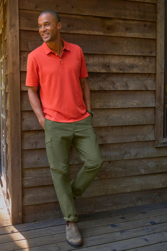 Man wearing red polo leaned up against the side of a building.