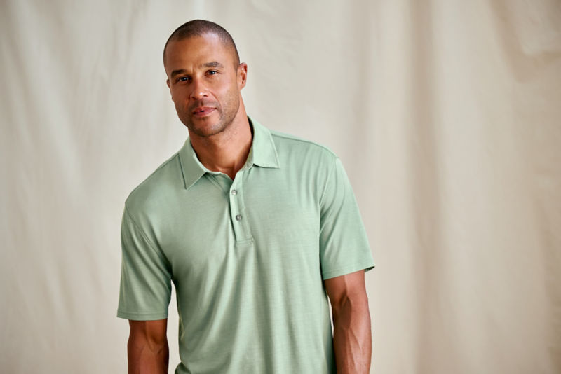 A model stands in front of a canvas drop cloth wearing a turquoise polo shirt.