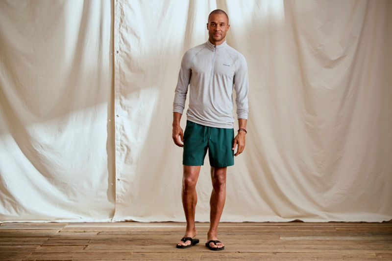A model stands in front of a canvas dropcloth wearing a gray technical tee.