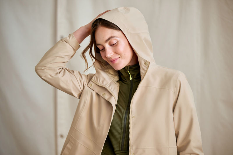 A model wearing a cream rain jacket with the hood on her head.