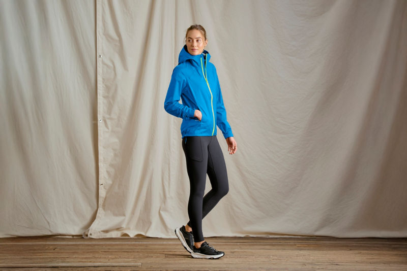 A model stands in front of a canvas dropcloth wearing a bright blue rain jacket.