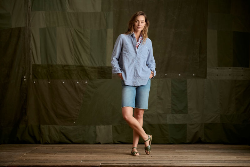 Woman wearing blue tunic and jean shorts in a studio.