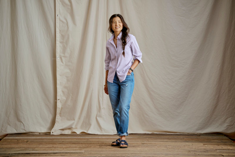 Woman wearing purple plaid shirt and jeans in a studio.