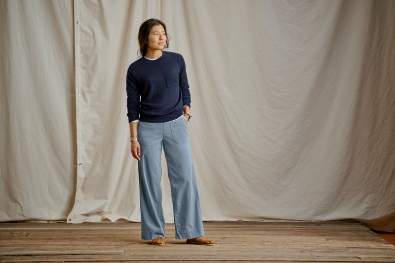 Woman wearing navy sweater and light blue wide legged pants in a studio.