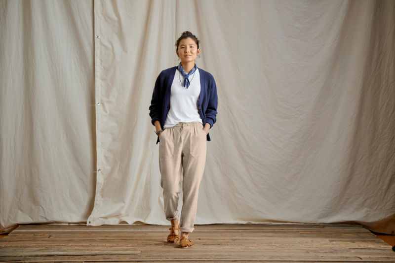 A waist-down view of a model wearing natural linen straight-leg pants rolled up at the cuff.