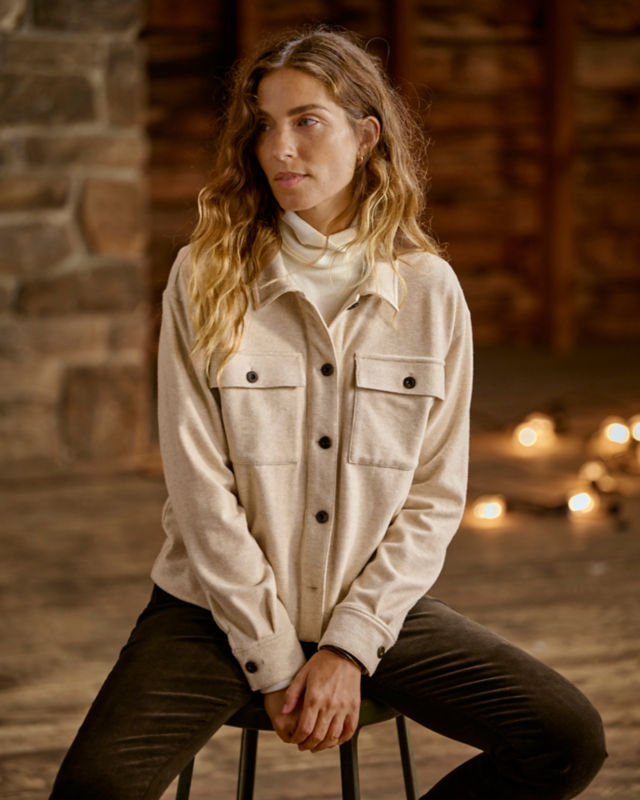 Woman wearing tan shirt jacket, turtleneck, and corduroys in studio.