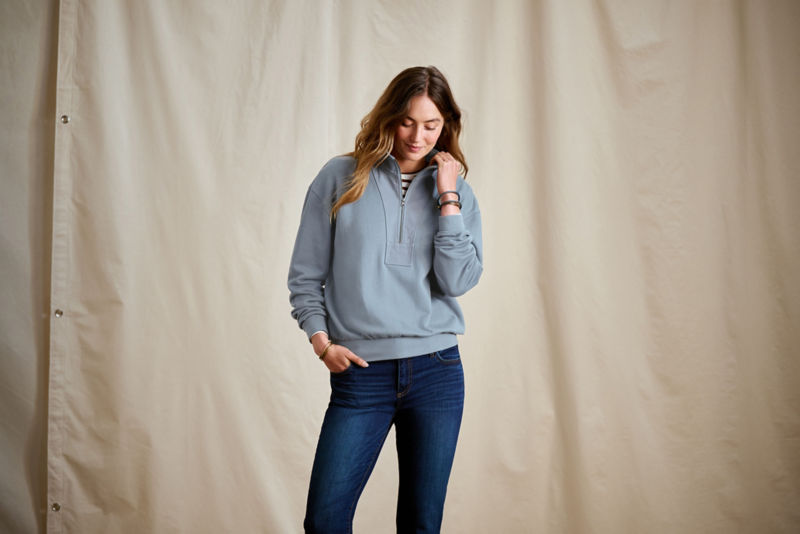 A woman wearing a blue pullover over a striped tee and jeans.
