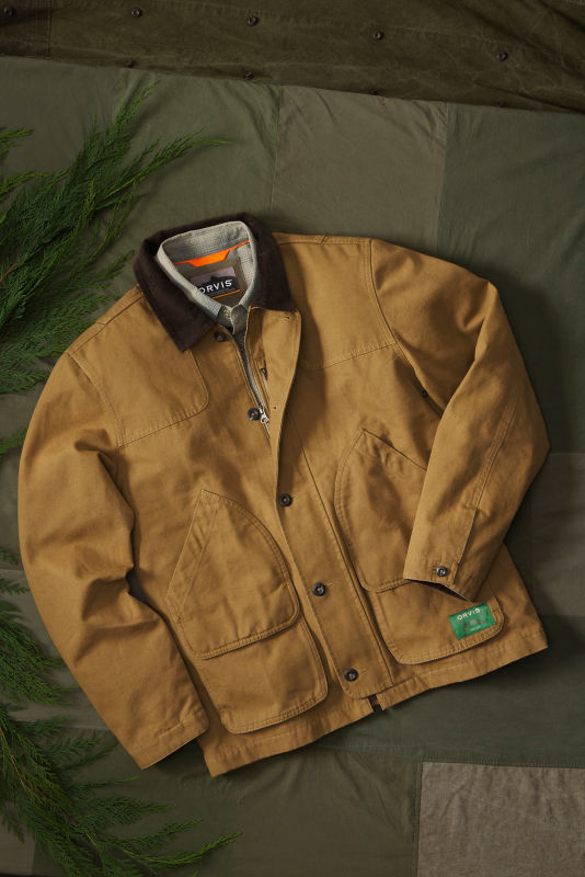 An Orvis chore coat laid out on a green cloth background.