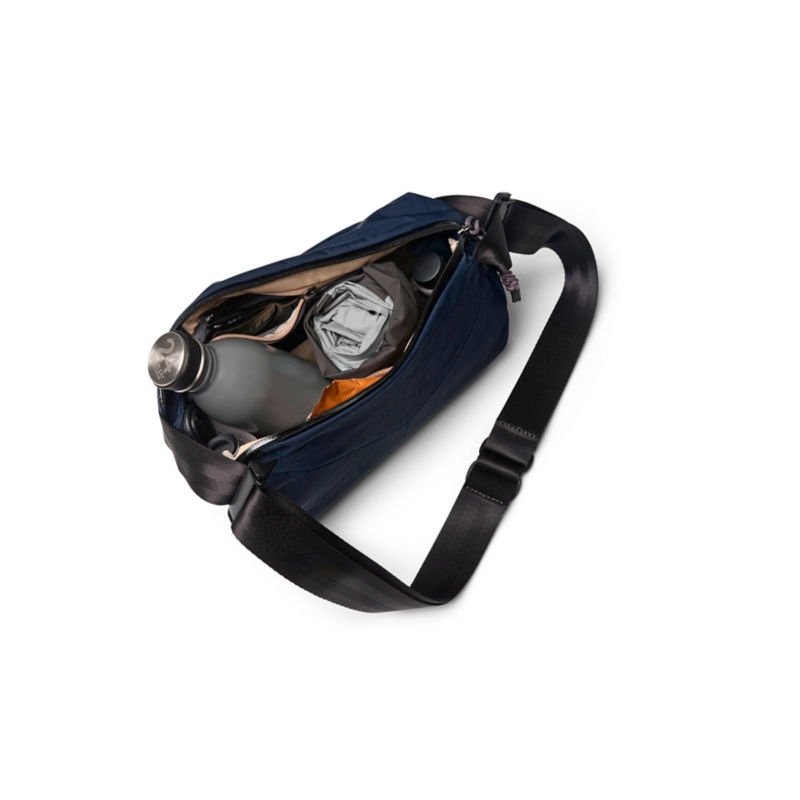 A packed navy-colored sling bag with water bottle, rain jacket, etc.