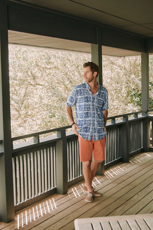 A waist-down view of a model in orange shorts on a wooden deck.