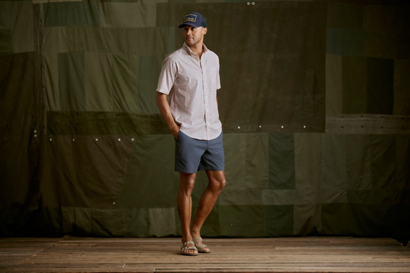 Man wearing red plaid shirt and grey shorts in a studio