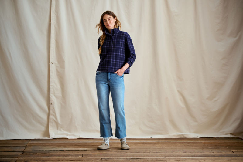 A woman wearing a blue plaid pullover with blue jeans.