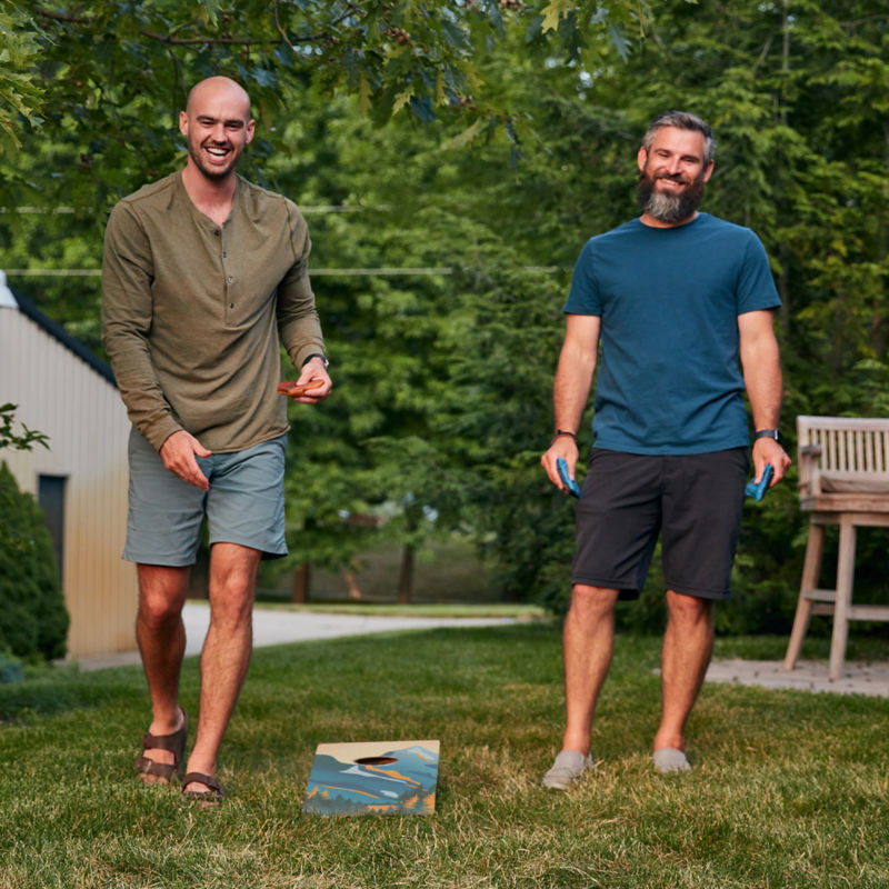 Two friends laughing and playing corn hole in the yard.