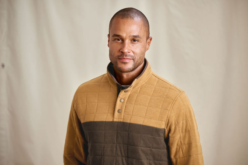 A waist-up view of a model wearing a color-blocked gold and chocolate quilted sweatshirt.