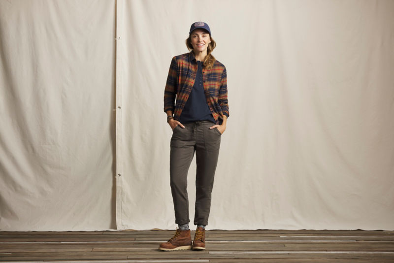 A model wearing a dark plaid shirt over grey pants and brown boots.