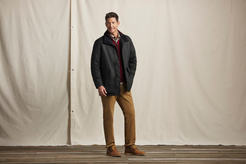 A model wearing a Barbour jacket over a red quarter-zip sweater and brown pants.