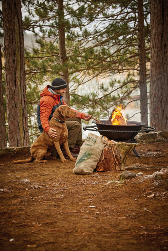 A man with his dog starting a campfire with fatwood kindling.