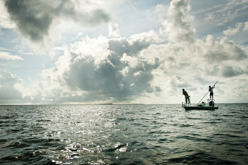 A fishing boat on the ocean under bright, cloudy skies.