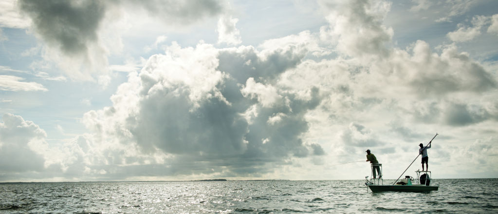 A fishing boat on the ocean under bright, cloudy skies.