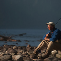 An angler sitting alone on rocky shoreline