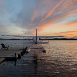 A float plane docked on vast flat water under a stunning sunset.