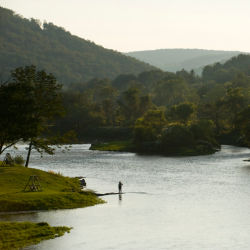 An angler standing in river while fishing among green hills.
