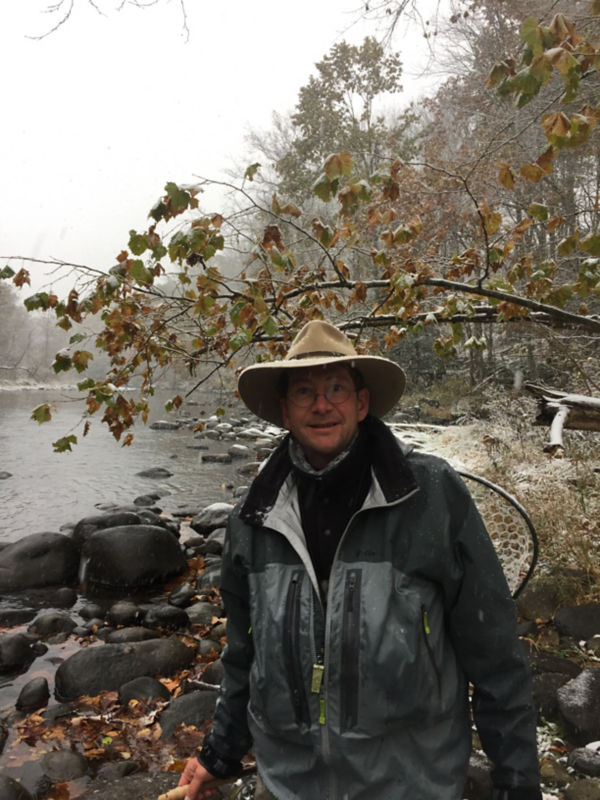 Fly Fishing Guide, Antoine Bissieux wearing waders stands next to a rocky river bank.