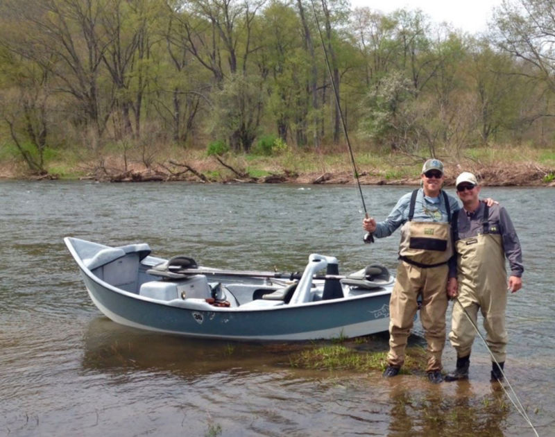 Two men standing side-by-side in front of a small boat