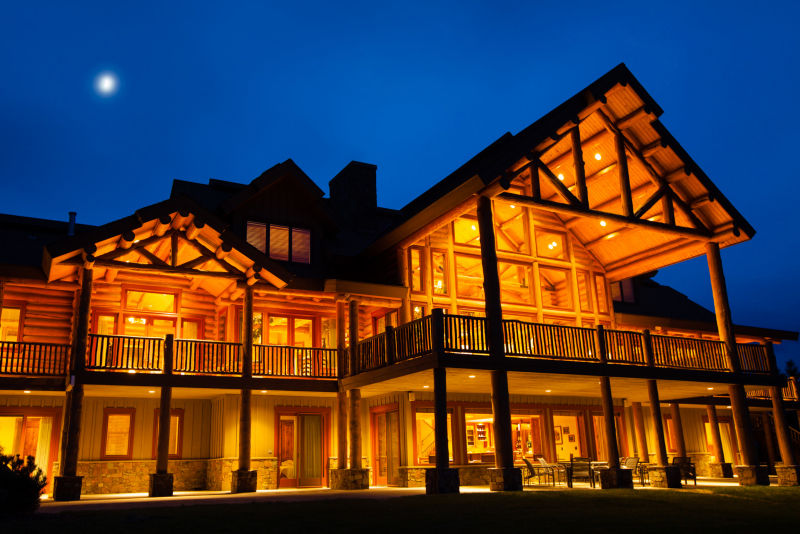 An evening shot of a large wooden lodge lit up under the night sky.