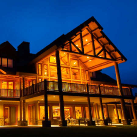 An evening shot of a large wooden lodge lit up under the night sky.
