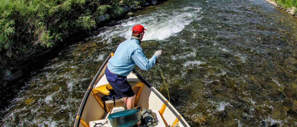 An angler casts a fly rod off of a rowboat on whitewater.