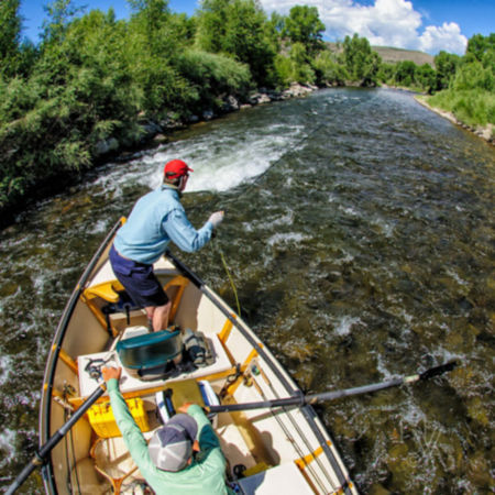 An angler casts a fly rod off of a rowboat on whitewater