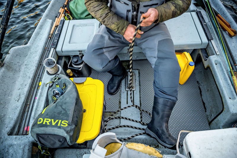 A man relaxes in the back of a small boat while wearing bootfoot waders.