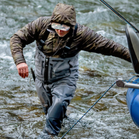 An angler in full winter gear wades through fast moving water