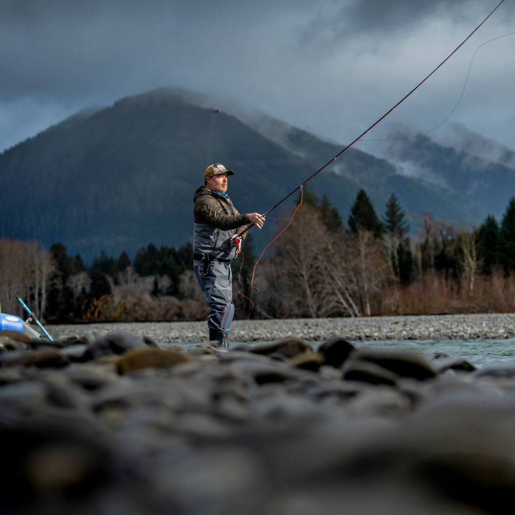 An angler dressed in full gear stands in a river while casting