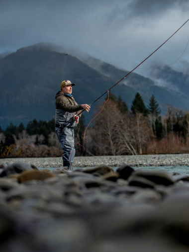 An angler casting for steelhead on a gray day in the mountains.