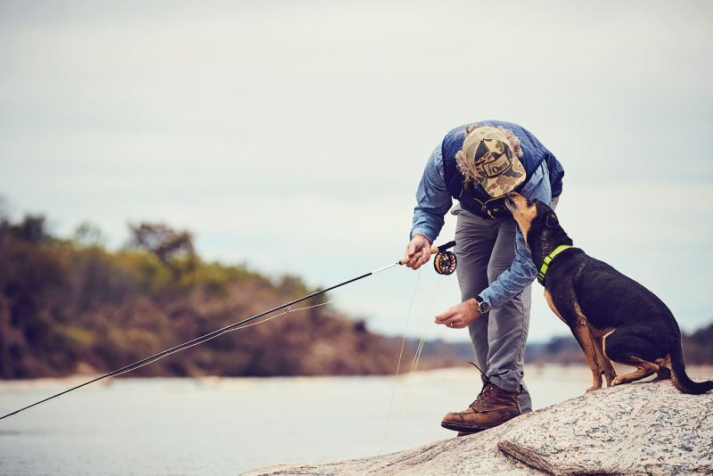 A man takes a moment from fly fishing to bend down and kiss his dog.