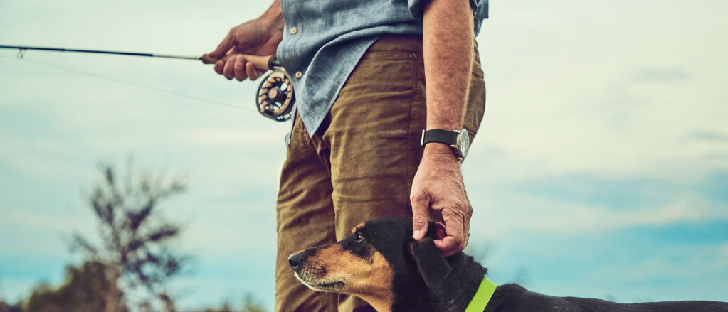Man holding a fly rod petting his dog