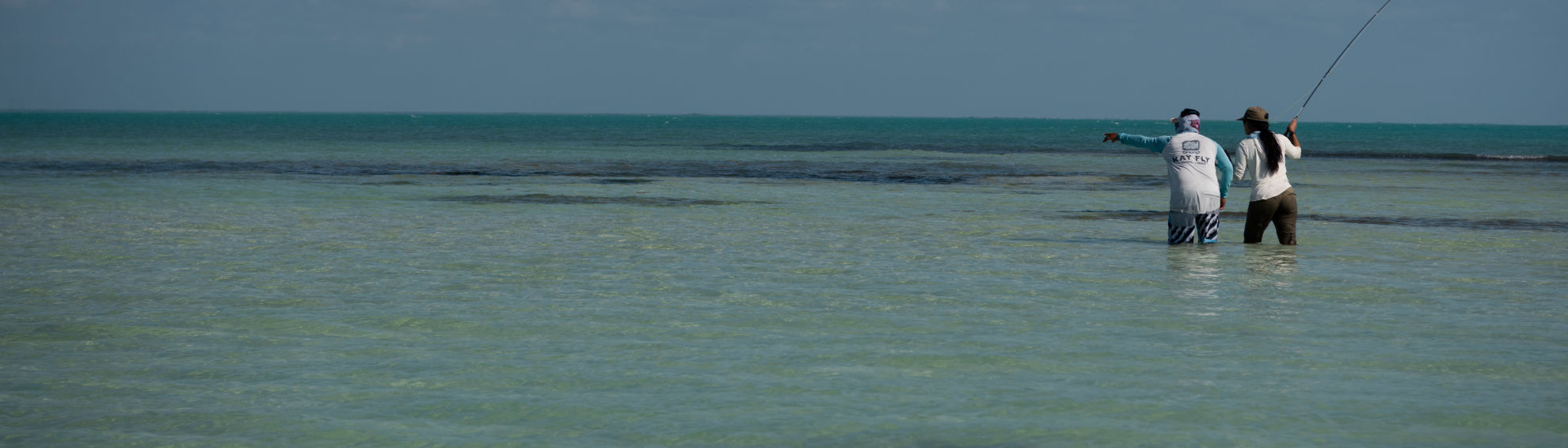 Two people wade into the flats off Belize casting for Permit.