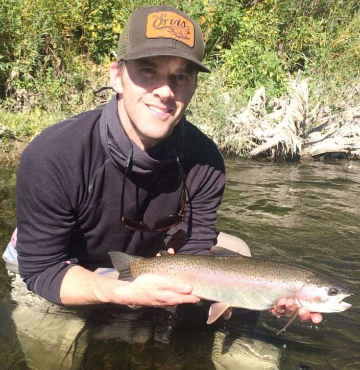 Adam Sigrist squatting in a river holding a fish