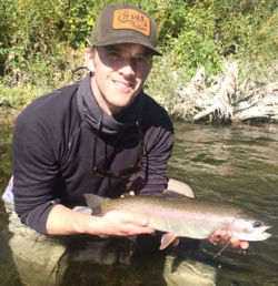 Adam Sigrist squatting in a river holding a fish