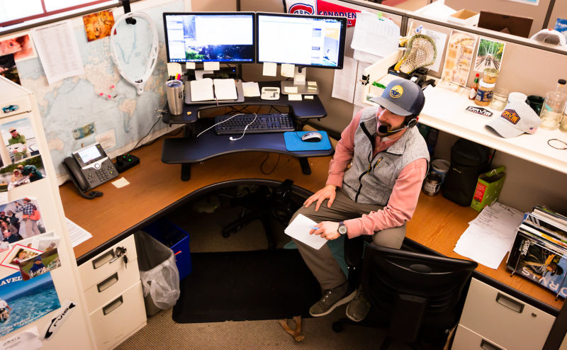 Seth sits on his desk in a busy cubicle at the Orvis Home Office.