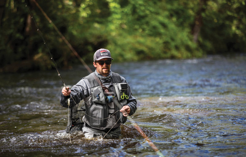 An angler casts while waist-deep in the river.