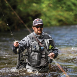 An angler casts from hip-deep in a river 
