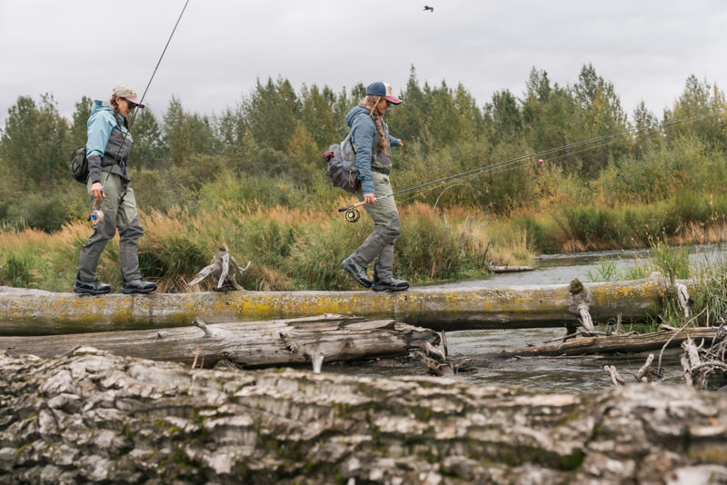 Two anglers walking on a log in the middle of the forest.