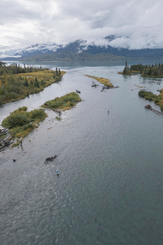 An aerial view of a lake with a man fishing in the forefront.
