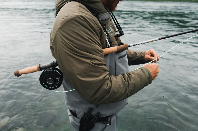 An angler tucks his Mission Spey Fly Rod under his arm to adjust his fly.