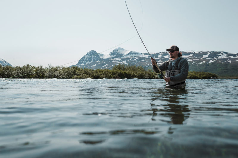 An angler casts his rod from waist-deep in vast waters.