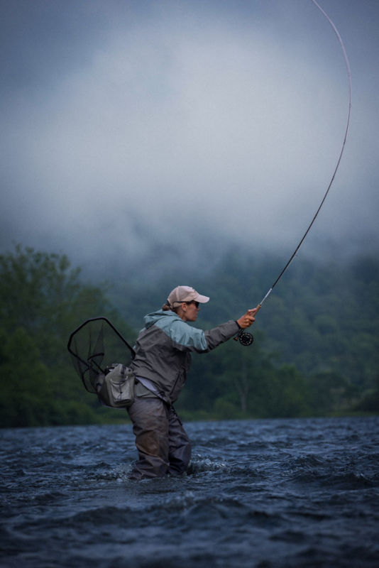 An angler wades through a choppy river in the rain.