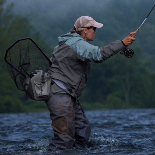 An angler wades through a choppy river in the rain.